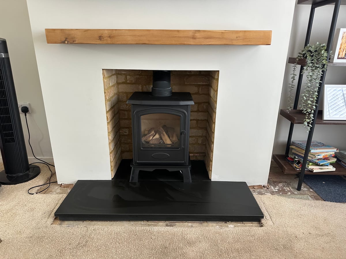 Finished fireplace with black stove, exposed brick and timber beam mantel